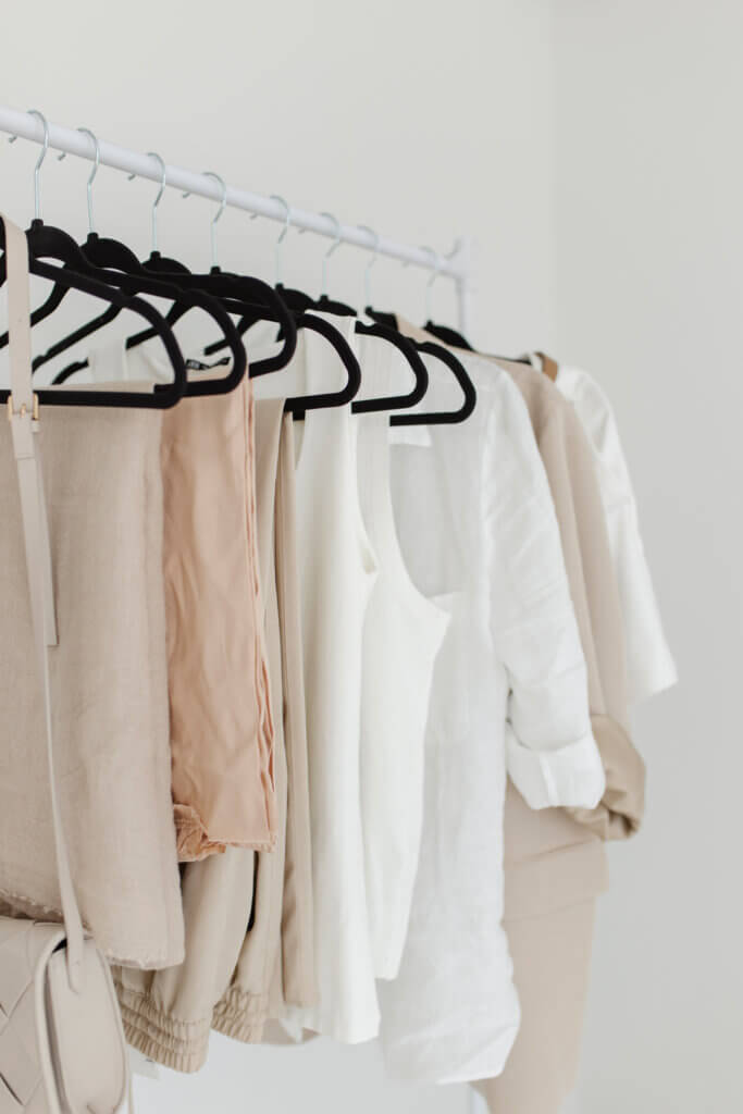picture of a minimalist closet with hanging clothes. Tan and white color clothes.