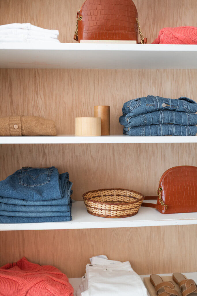 picture of folded clothes and purses on a white shelf.